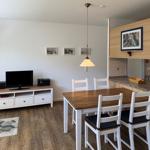 Essbereich mit Tisch und Stühlen, Küche und Wohnbereich mit Fernseher und Wandbildern.