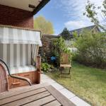 Terrasse mit Liege, Tisch und Stuhl im Garten. Hintergrund: Gras, Bäume und Haus.