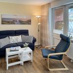 Ein Wohnzimmer mit Sofa, Sessel, Tisch und Fensterblick.