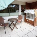 Terrasse mit Tisch, zwei Stühlen und Strandkorb. Hintergrund: Glasfront und Backsteinmauer.