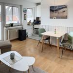 Living and dining area with table, chairs, and windows. Kitchen with worktop and appliances.