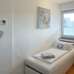 A bedroom with a single bed, wall art, and window overlooking the street.