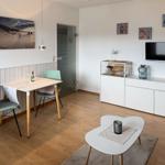 Living room with dining table, TV, and white cabinets. Wooden floor and wall picture.