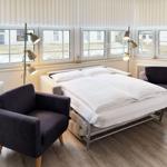 Schlafzimmer mit Bett, zwei Sesseln und Fenstern mit Blick nach draußen.