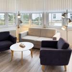 Wohnzimmer mit Sofa und zwei Sesseln, runder Tisch und Fenster mit Blick nach draußen.