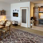 Living area with dining space, kitchen, and TV. Wooden furniture and carpeted floor.