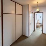 Hallway with closet, door, and lamp. In the background, a dining area with chairs is visible.