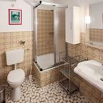 Bathroom with shower, sink and toilet. Tiles on walls and floor.