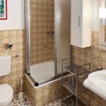 Bathroom with shower, sink, and toilet. Walls tiled with pattern.