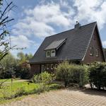 Ein zweistöckiges Haus mit dunklem Dach und rotem Backstein. Vorgarten mit Rasen und Pflanzen.