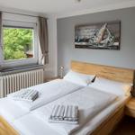 Schlafzimmer mit Holzbett, Fensterblick auf Wald und Wandbild mit Segelboot.