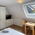 Zimmer mit Dachschrägen, Bett, Kleiderschrank, TV und kleinem Holztisch mit zwei Stühlen.