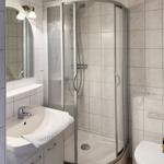 Badezimmer mit Duschkabine, Waschbecken und Toilette. Fliesenwand und Spiegel.