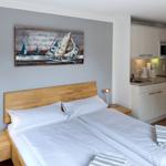 Schlafzimmer mit Doppelbett, Küchenzeile und Wandbild mit Segelbooten.