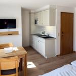 Küche mit Spüle, Mikrowelle und Arbeitsplatte. Essbereich mit Tisch und Stühlen. Fernseher an der Wand.