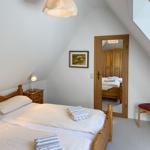 Schlafzimmer mit Holzbett, Nachttisch, Stuhl und Spiegel. Dachschräge und Fenster sichtbar.