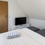 Schlafzimmer mit Doppelbett, Fernseher und grauen Sitzkissen.