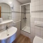 Badezimmer mit Dusche, Waschbecken und Toilette. Fliesenwand und Holzfußboden.