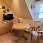 Ein Raum mit Holztisch, zwei Stühlen, Fernseher und Fenster mit Vorhängen.