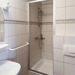 Badezimmer mit Dusche, Waschbecken und Toilette. Fliesenwand mit dekorativer Bordüre.
