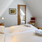 Schlafzimmer mit Dachschrägen, Bett, Stuhl und Bild an der Wand.