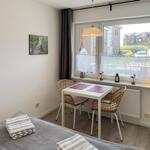 Room with table, two chairs, and bed. Window with view of residential area.