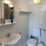 Bathroom with sink, toilet, and mirror. White tiles and modern lighting.