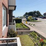 Red brick house with balcony, view of parking lot and green areas.