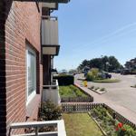 View from balcony onto street with parking lot and trees under blue sky.