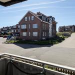 Villa with balcony, parking lot, and adjacent houses under blue sky.