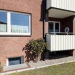 Red brick house with balcony and windows. Grass and shrubs in the front garden.
