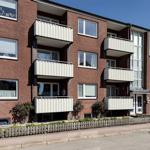 Red brick building with balconies and windows. Front garden with fence.