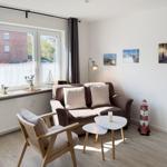 Living room with sofa, chair, and table. Window with view of buildings. Wall art and lighthouse figurine.