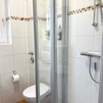 Bad mit Dusche, Toilette und Fenster. Fliesen mit Mosaikstreifen.