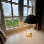Schreibtisch mit Lampe vor Fenster mit Blick auf Grün und Dach