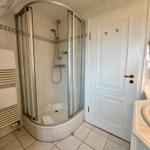 Badezimmer mit Duschkabine, Waschtisch und Heizung. Fliesenboden und weiße Wände.