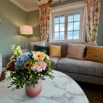 Ein Wohnzimmer mit Sofa, Blumen und Fenster. Die Wände sind hellgrün.