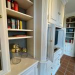 Weißer Schrank mit offenen Regalen, Fernseher und Glasbehältern auf Holzfußboden.