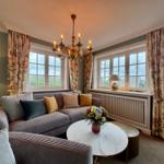 Ein Wohnzimmer mit Sofa, runden Tisch und Fenstern mit floralen Vorhängen.