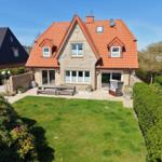 Haus mit rotem Dach, Garten und Terrasse mit Tisch und Stühlen.