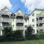 Haus mit mehreren Balkonen und grüner Umgebung unter blauem Himmel.