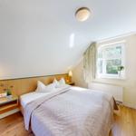 Ein Schlafzimmer mit Dachschrägen, Bett, Nachttisch und Fenster mit Blick auf Bäume.