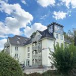 Haus mit Balkonen und Dachterrasse unter blauem Himmel mit weißen Wolken.