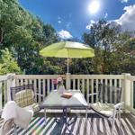 Terrasse mit Tisch, zwei Stühlen und Sonnenschirm. Blick in einen grünen Wald.