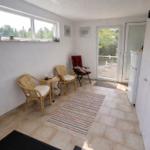 Raum mit Sitzgelegenheiten, Fenster und Glastür zur Terrasse. Fliesenboden und Teppich.