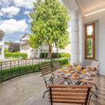 Terrasse mit Tisch, Stühlen und Frühstück. Blick auf grüne Bäume und weiße Gebäude.