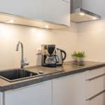 Küche mit Spüle, Kaffeemaschine und Kanne auf dunkler Arbeitsplatte.