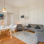 Wohn- und Essbereich mit grauem Sofa, weißen Stühlen und Holzboden.