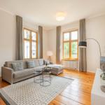 Wohnzimmer mit Sofa, zwei Fenstern, Holzboden und TV-Schrank.