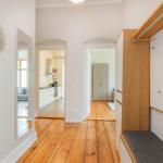 Flur mit Holzboden, Spiegeln und Kleiderschrank. Küche und Schlafzimmer sind sichtbar.